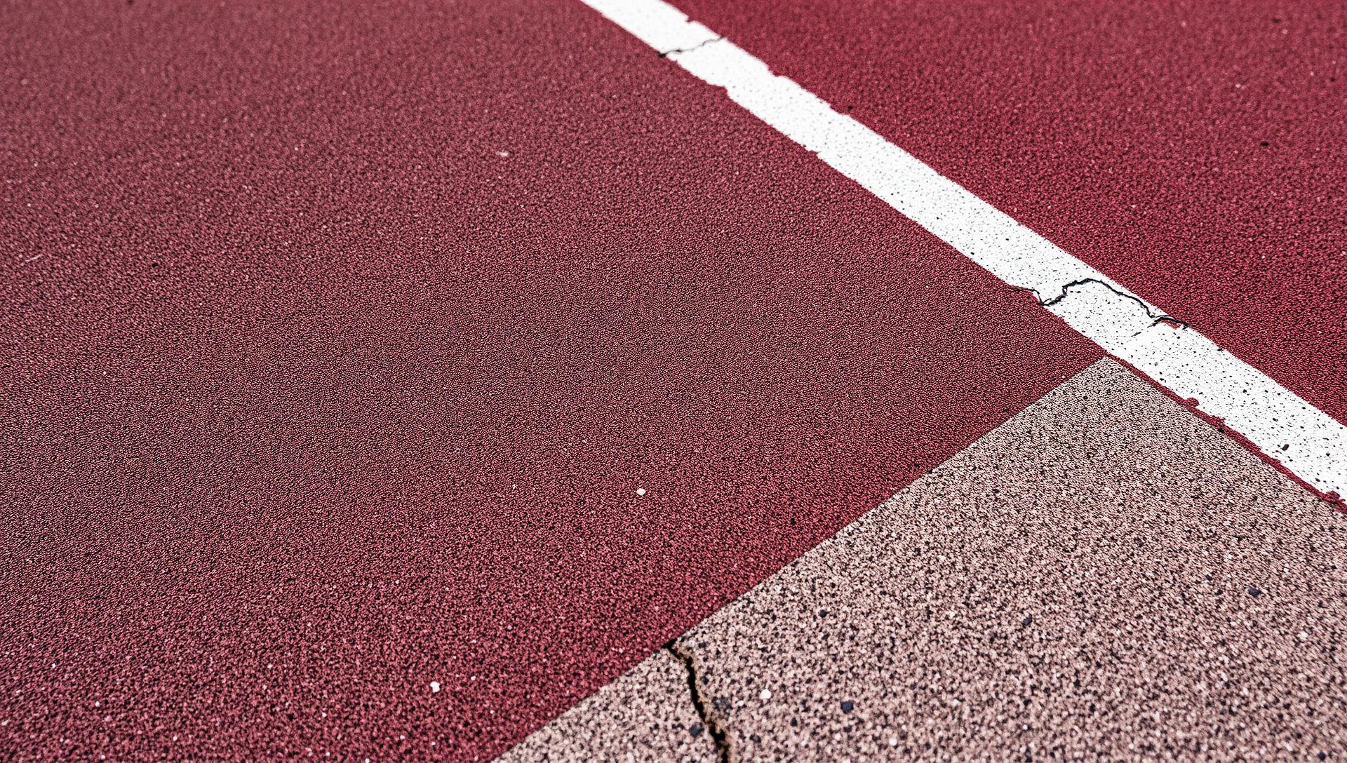 Macro texture of a weathered athletic track surface with a faded white lane line meeting concrete
